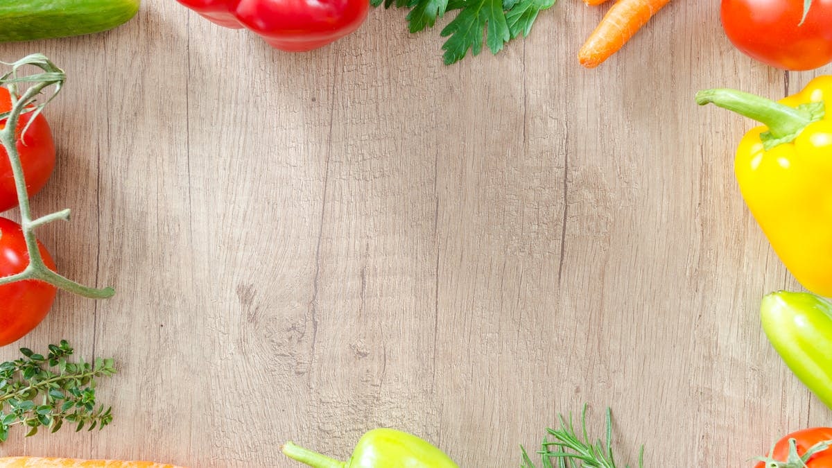 A top view of various fresh organic vegetables arranged on a rustic wooden surface.